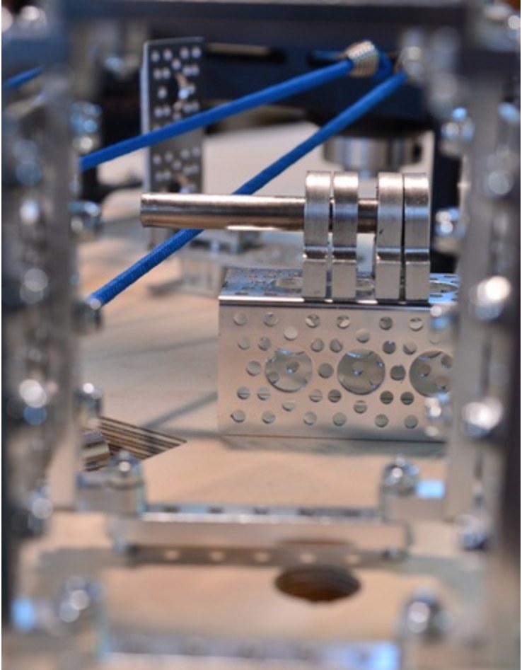 Close-up photograph of a machined art-machine joint in polished aluminium with blue elastic cord under tension